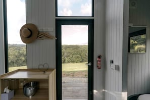 A room with a wooden table, a hat on the wall, a fire extinguisher, and a view of a forest. - Tiny House for Outdoor Adventure near Glacier Rock in Cairns, Queensland (Kuranda)