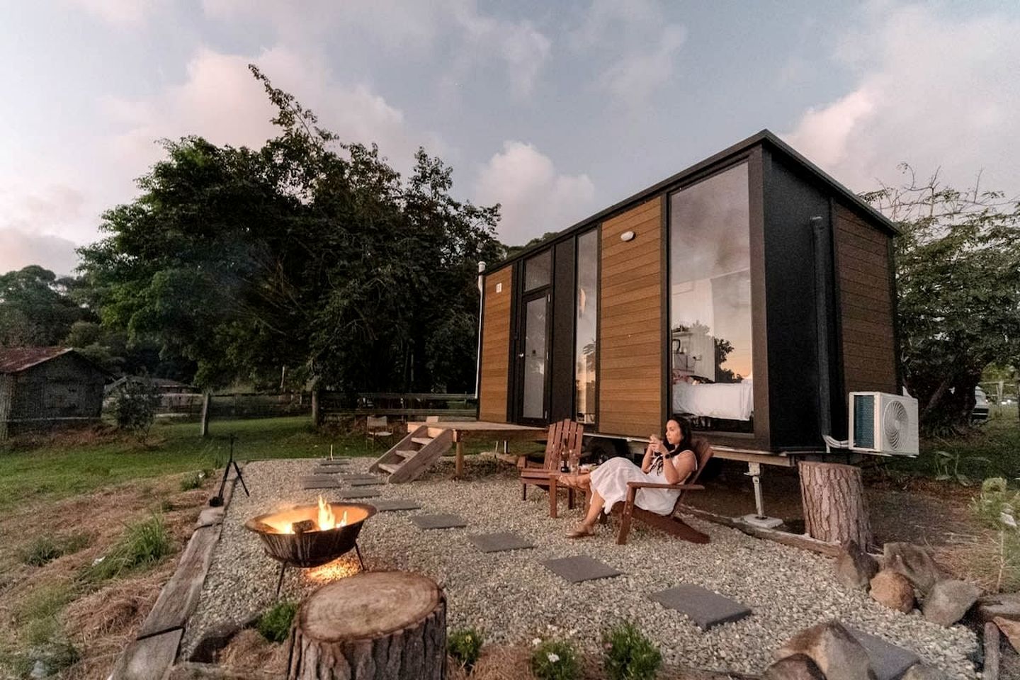 Een moderne blokhut met een vuurkuil, buitenmeubels en een groot raam met uitzicht op een natuurlandschap.