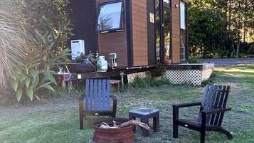 A modern cabin with a deck, outdoor seating, and a fire pit.
