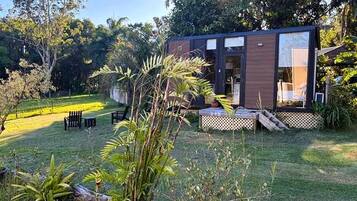 Een modern huis met een terras, omgeven door weelderige begroeiing en een verzorgd gazon.