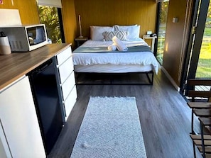 A compact bedroom with a bed, bedside table, and a microwave on a counter. - Sunshine Coast Glamping in a Tiny House for a Nature Escape in Queensland (Palmwoods)