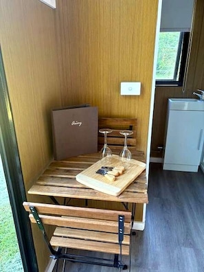 A compact kitchen with a wooden table, a wine glass, and a cutting board. - Sunshine Coast Glamping in a Tiny House for a Nature Escape in Queensland (Palmwoods)
