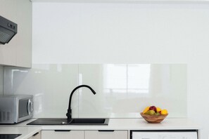A kitchen with a microwave, a sink with a black faucet, and a bowl of fruit on the countertop. - Serene 2BR Mackenzie Apt 5 Min Walk to the Beach (Larnaka)