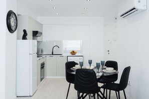 A modern kitchen with white cabinetry, a built-in oven, and a dining area with black chairs and a glass table set for four. - Serene 2BR Mackenzie Apt 5 Min Walk to the Beach (Larnaka)