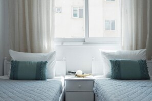 Quarto de hotel com duas camas, mesa de cabeceira e janela com cortinas.