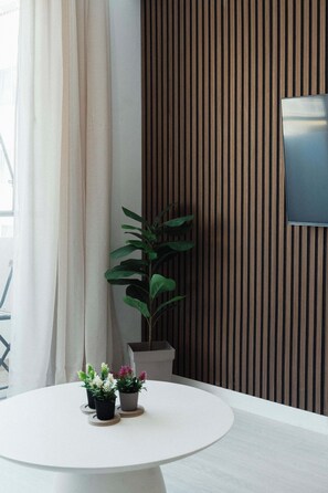 A modern room with a round white table, a potted plant, and a flat-screen TV mounted on a wooden wall. - Serene 2BR Mackenzie Apt 5 Min Walk to the Beach (Larnaka)