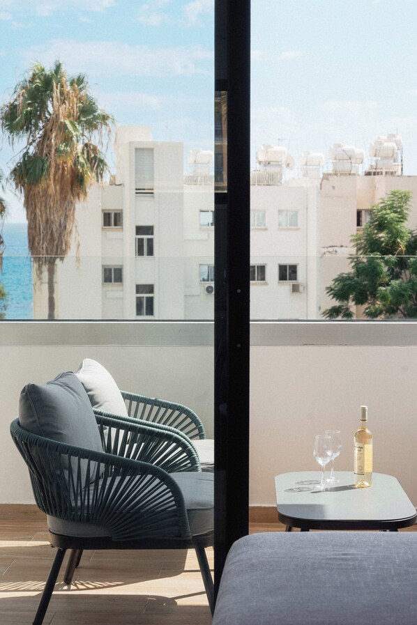 Un balcon avec une chaise et une petite table, d’où l’on a vue sur un immeuble et la mer.