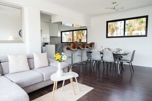 A modern living room with a grey sofa, a dining area with a table set for four, and a kitchen in the background. - Beautiful 2BR Sea View Apt with Dedicated Office (Agios Tychonas)