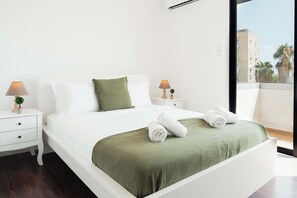 A hotel room with a bed, two bedside tables, a window with a view, and a balcony. - Beautiful 2BR Sea View Apt with Dedicated Office (Agios Tychonas)