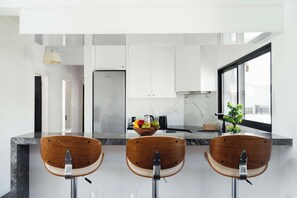 A modern kitchen with white cabinets, a stainless steel refrigerator, a black countertop, and a window with a view. - Beautiful 2BR Sea View Apt with Dedicated Office (Agios Tychonas)