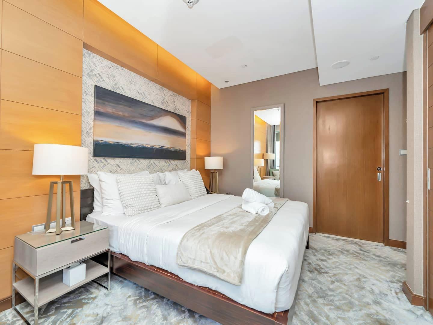 Une chambre d’hôtel avec un grand lit, des lampes de chevet, une table de nuit, un sol à motifs de marbre et un grand tableau au mur.