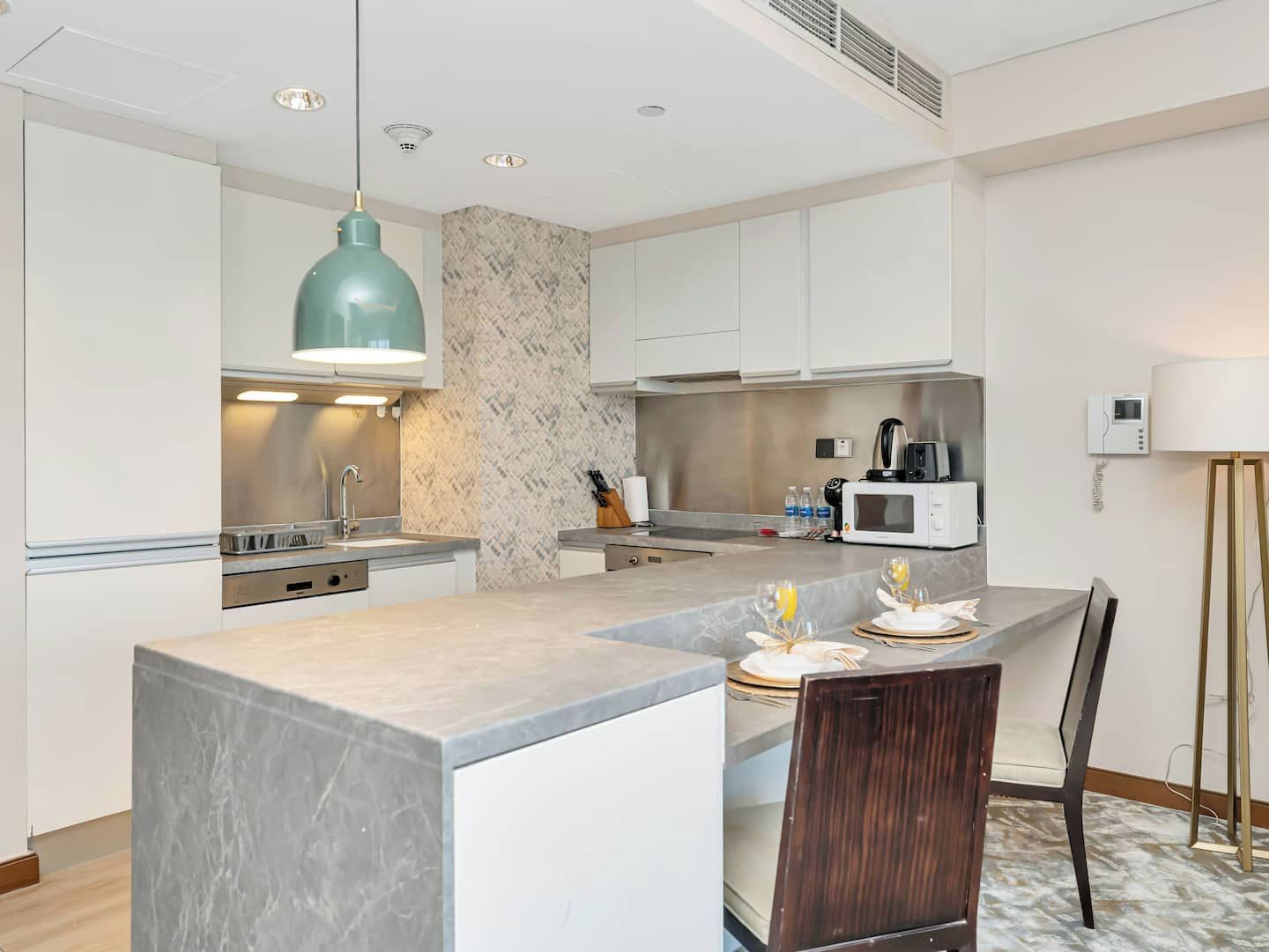 A modern kitchen with a marble island, white cabinets, a pendant light, and a microwave.
