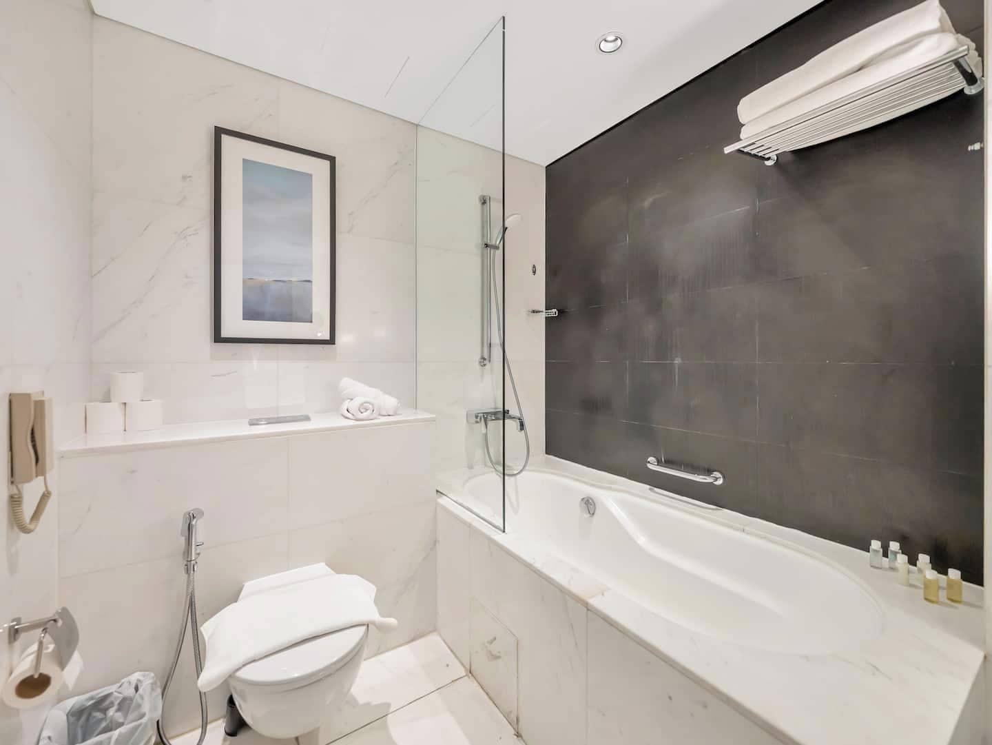 A modern bathroom with a bathtub, a shower, and a toilet. There is a framed picture on the wall and a towel rack.