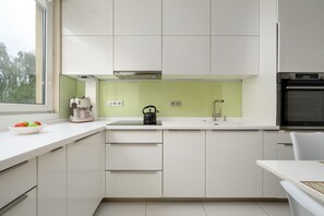 A modern kitchen with white cabinets, a green backsplash, a kettle, and a coffee maker on the counter. - Wroclaw | 29 Budziszyńska | Bright Apartment | Coffee machine (Wrocław)