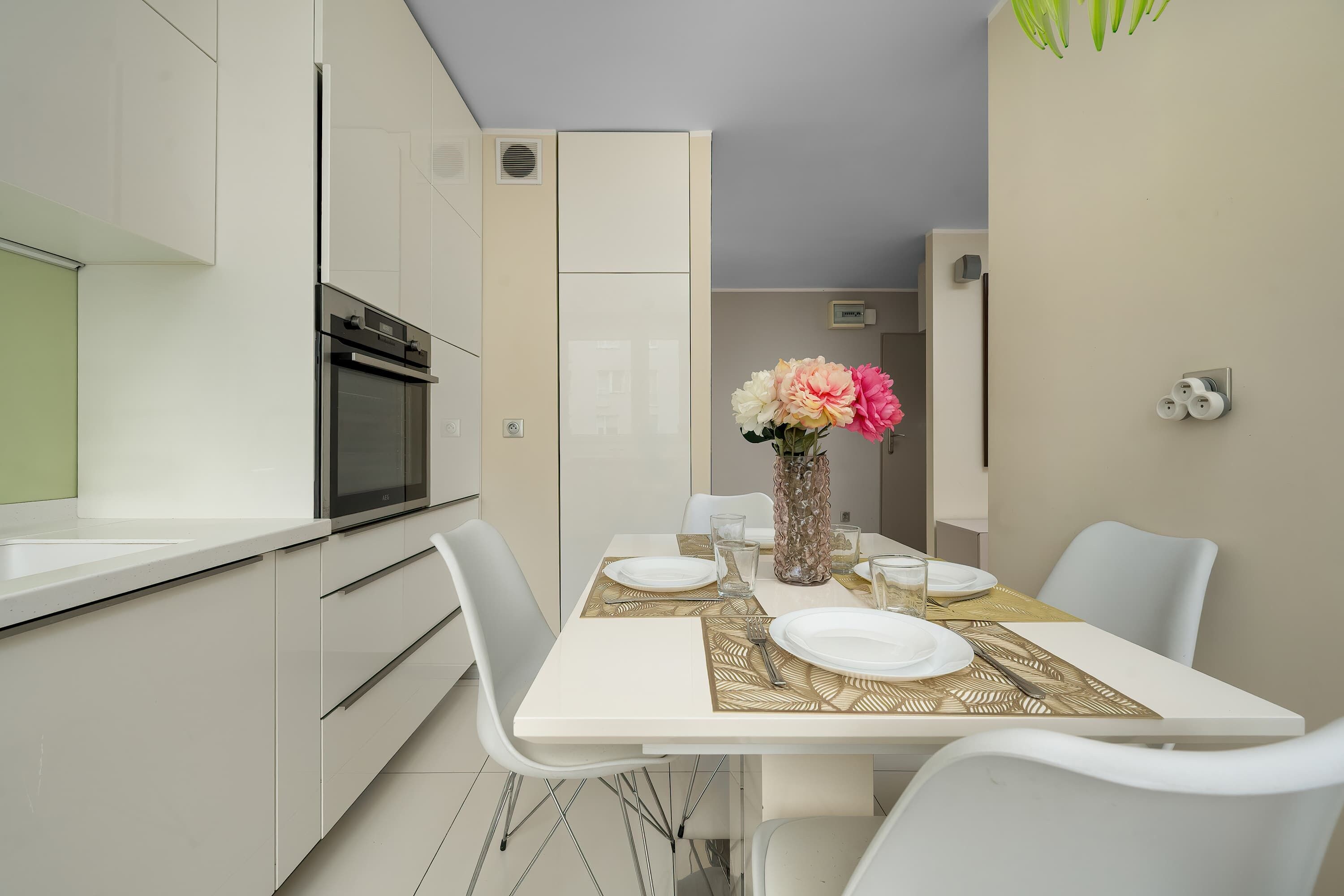 A modern kitchen with white cabinetry, a built-in oven, and a dining area with a white table set for four.