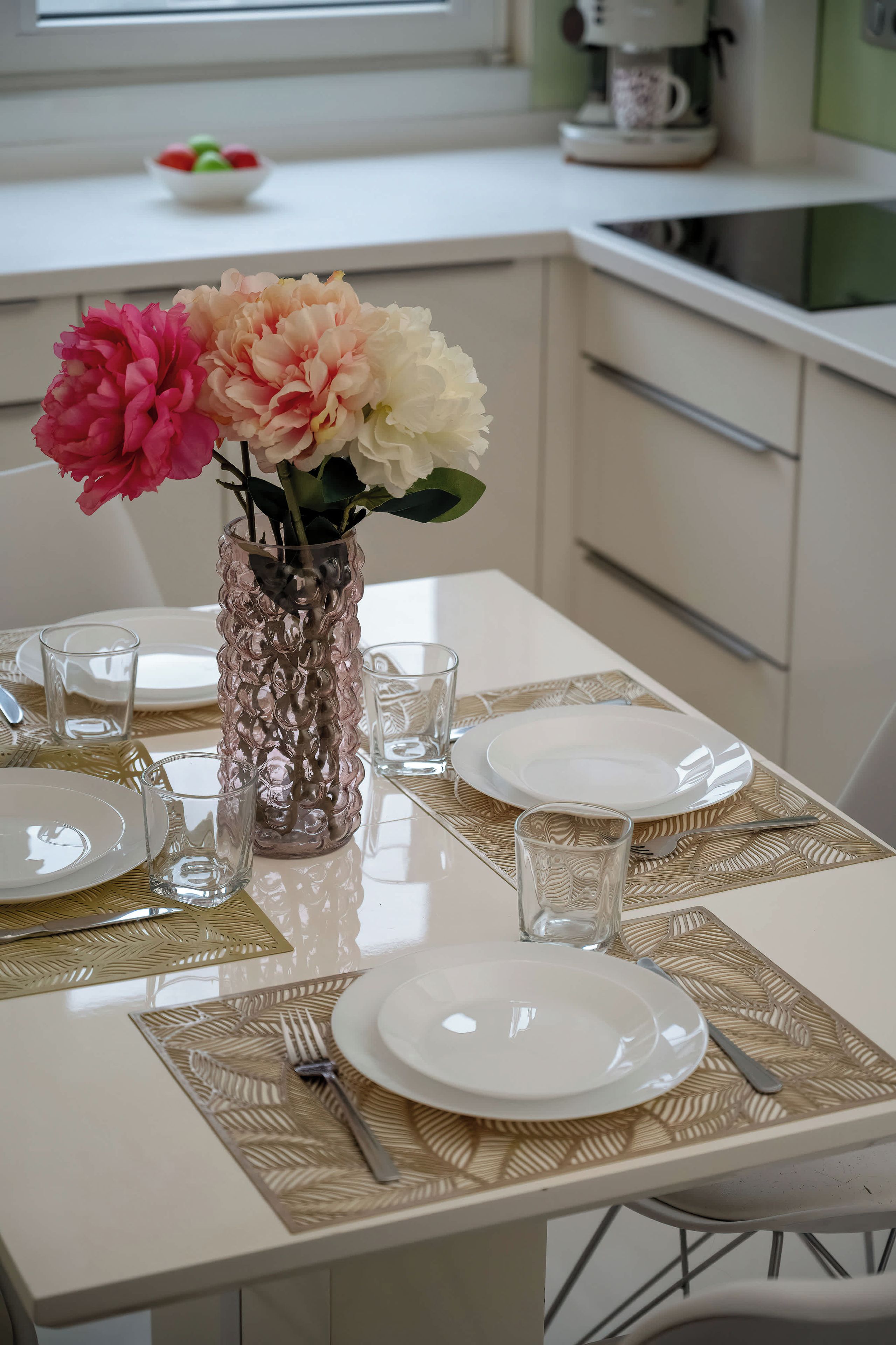 Una mesa de comedor servida con platos, cubiertos y un florero con flores.