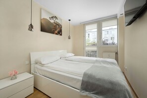 Ein Schlafzimmer mit einem Bett, einem Nachttisch und einem Fenster mit Blick auf Gebäude.