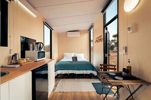 Habitación pequeña con cama, kitchenette y una mesita.