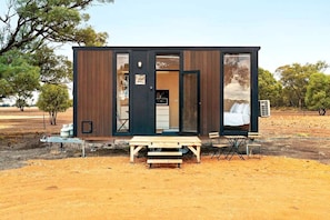 Una cabaña pequeña y moderna con fachada de madera, una banca y una mesa en el exterior.