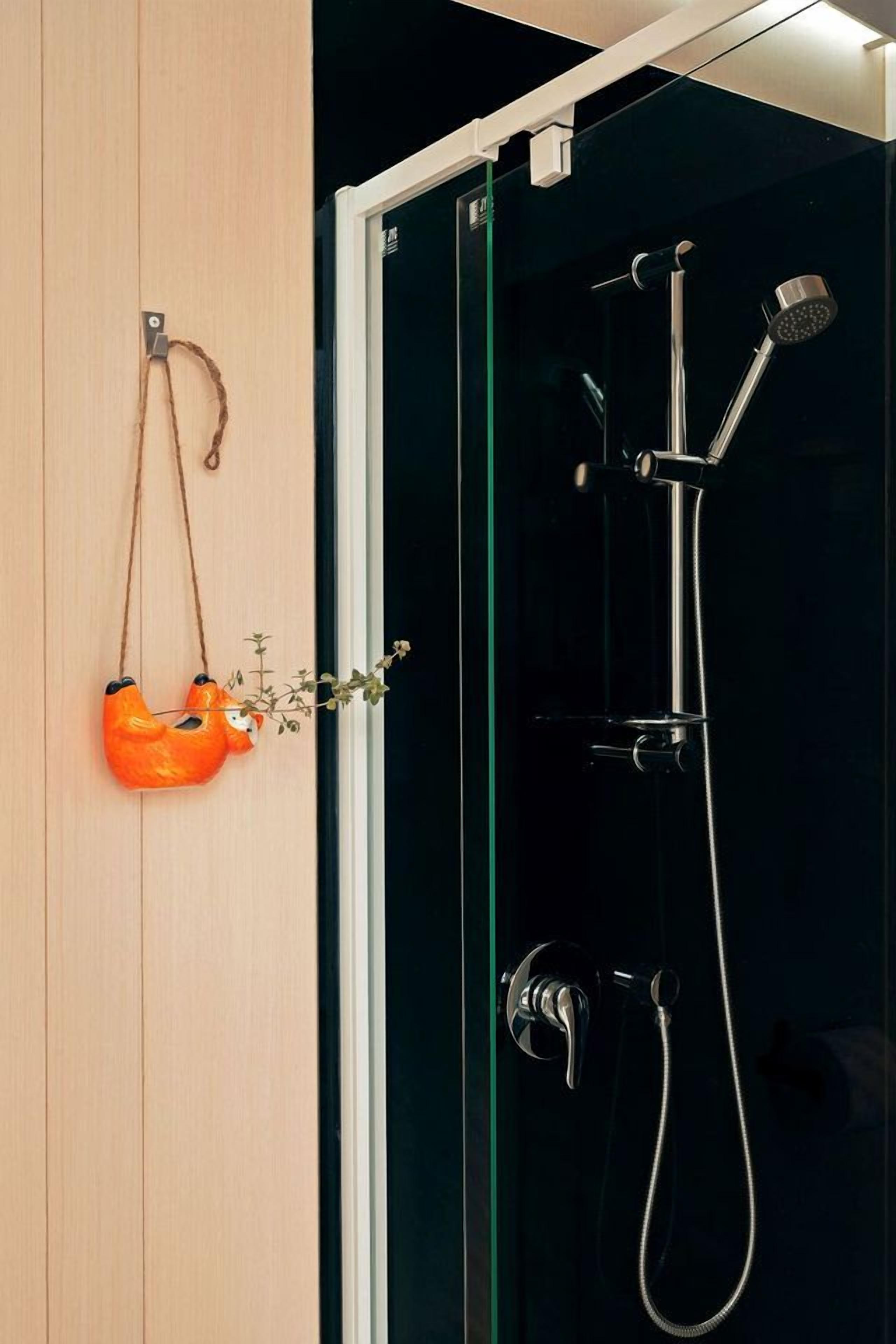 Ein Badezimmer mit Duschkabine aus Glas, einer Holztür und einem hängenden, orangefarbenen Pflanzgefäß mit Pflanze.