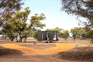 Una casa móvil de un piso con techo plano, ubicada sobre terreno de tierra y cielo despejado.