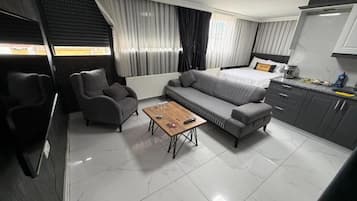 A modern hotel room with a sofa, a small table, a bed, and a kitchenette.