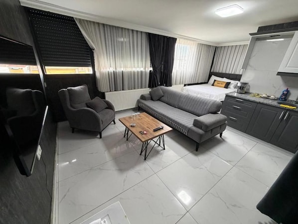 A modern hotel room with a sofa, a small table, a bed, and a kitchenette. - Çınar Suit Hotel (Buca)