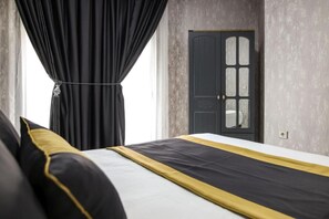 Habitación de hotel con cama, cortinas negras, una puerta con paneles de vidrio y pared con textura.
