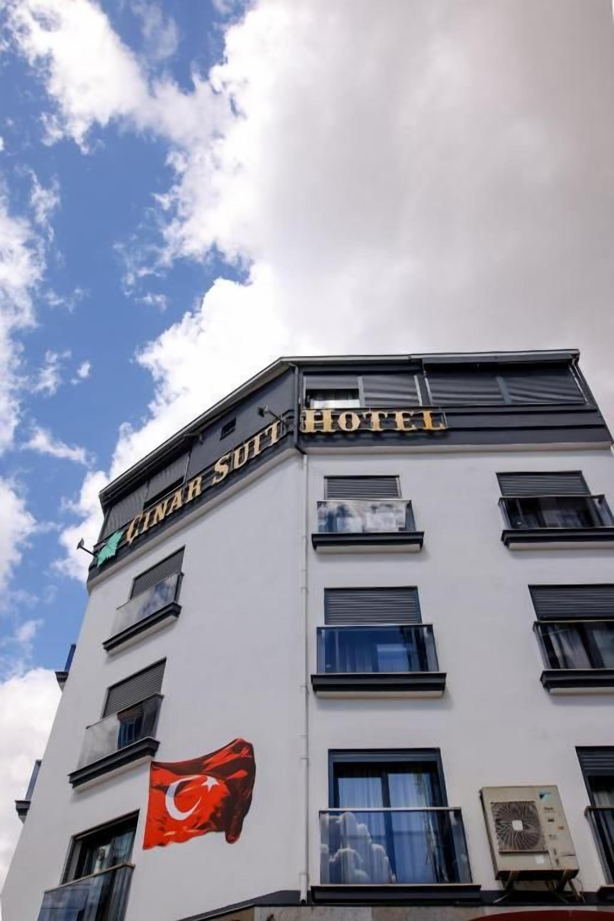 Edifício de hotel com uma placa que diz 'CINAR SUIT HOTEL' e uma bandeira com uma lua crescente e uma estrela.