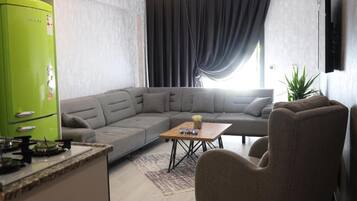 A modern living room with a sectional sofa, a green refrigerator, a wooden coffee table, and a TV mounted on the wall.