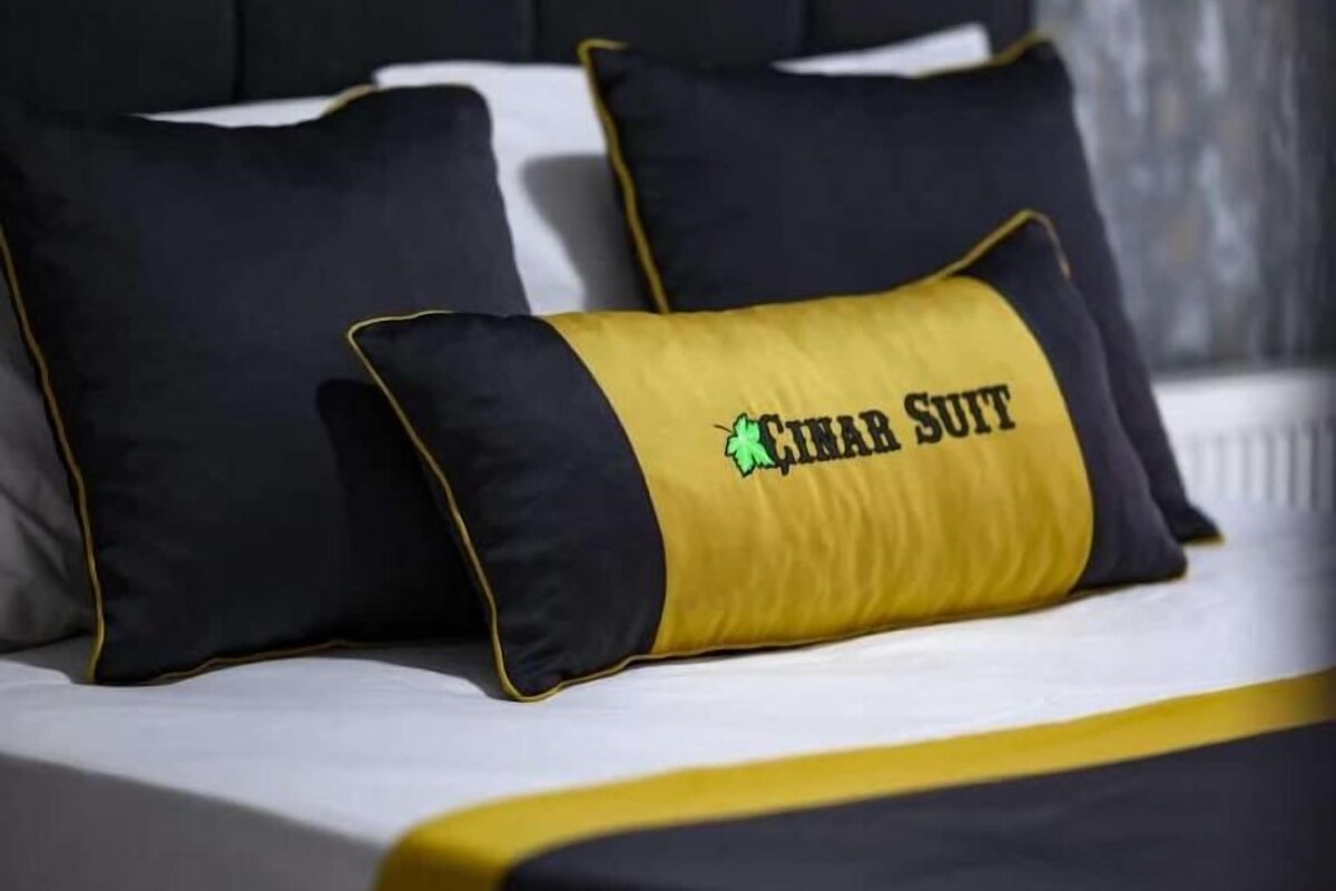 Un llit amb roba de llit negra i groga, incloent nassos amb el text 'HINAR SUIT'.