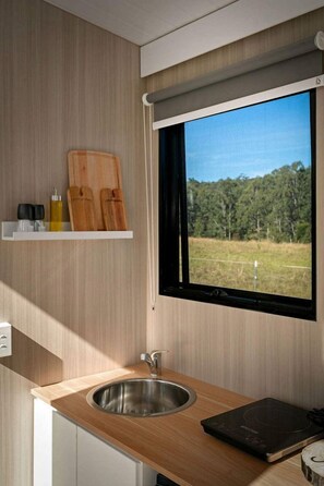 A modern kitchen with a stainless steel sink, wooden countertop, and a window with a view of a forest.