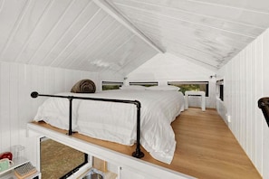 A compact, single-room cabin with a loft-style bed, a small kitchenette, and a view through a window.