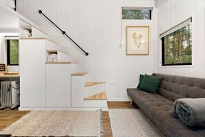 A modern living room with a staircase, a sofa, and a framed picture on the wall.