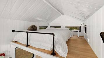 Uma cabana compacta, com um único quarto, cama no estilo beliche, uma pequena cozinha e vista pela janela.