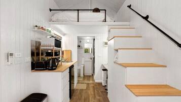 A compact, white-themed interior with a kitchenette, a small dining area, and a staircase.