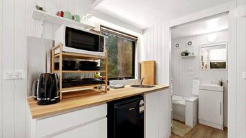 Una cocina compacta con microondas, hervidor y estantes de madera.