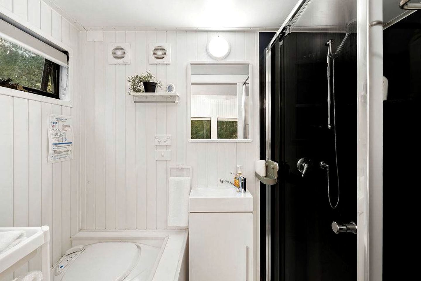 Une salle de bain avec une baignoire, un lavabo, un miroir, une douche et une plante en pot.