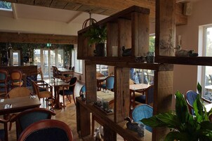 A restaurant interior with wooden furniture and decor, including a high wooden shelf with plants and decorative items.