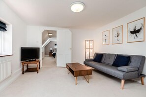 A modern living room with a grey sofa, a wooden coffee table, a TV on a stand, and framed artwork on the wall.