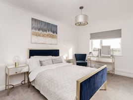 A bedroom with a bed, bedside tables, a desk, a chair, a window, and a painting on the wall.