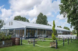 A greenhouse structure with a glass roof, surrounded by picnic tables and a white picket fence.