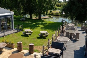A deck with outdoor seating, a pond, and a building with a covered area.