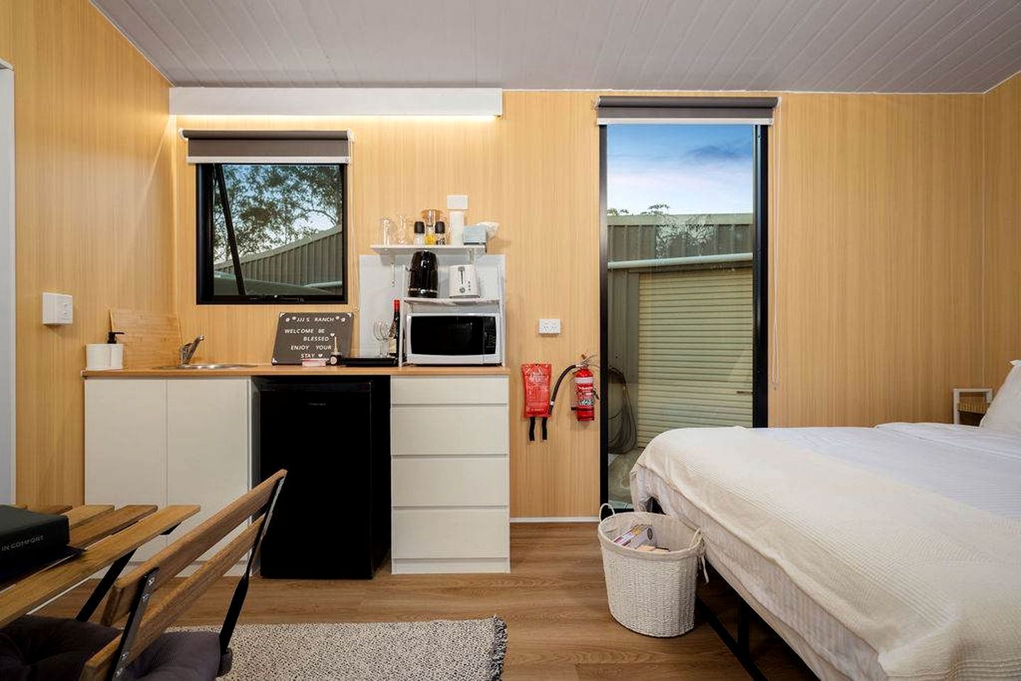 Une pièce de taille modeste comprenant un lit, une petite kitchenette, une fenêtre et un extincteur.