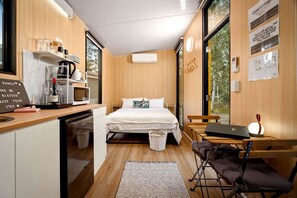 Una camera compatta con un letto, una scrivania, una sedia, un forno a microonde e un piccolo lavandino.