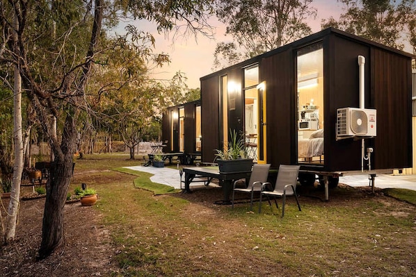 A modern, compact mobile home with large windows, a dining area, and a patio.