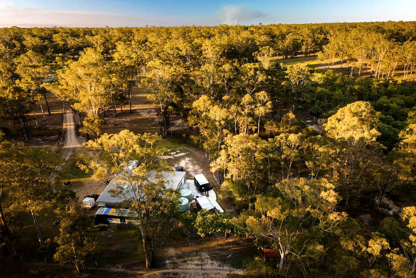 A rural property with a fenced area, a building with a flat roof, and a dirt road.