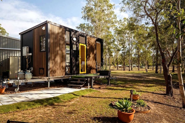 A modern, compact house with a deck and outdoor seating area, surrounded by trees.