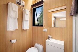 A bathroom with a toilet, sink, and window. There are towels hanging on a rack and a mirror above the sink.
