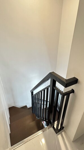 A staircase with a black metal railing and a white wall.